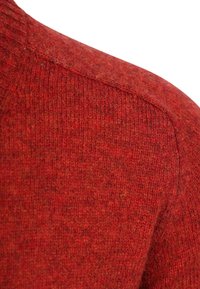 Nahaufnahme von rotem Strickstoff, der die detaillierte Textur und das Stichmuster an einer Schulternaht zeigt.