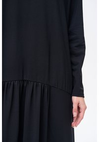Czarna sukienka z długim rękawem, z marszczonym pasem i zwiewnym dołem. Wykonana z miękkiej tkaniny, charakteryzuje się gładką fakturą i minimalistycznym designem.