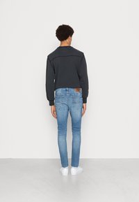 Sudadera negra de manga larga con un acabado texturizado, combinada con jeans ajustados de color azul claro y zapatillas blancas, vista desde atrás.