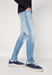 Ljusblåa jeans i denim med en urtvättad design, rak passform och subtila slitningar, kombinerat med mörkblå sneakers med vita detaljer.