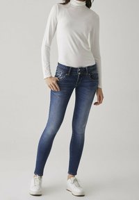 Tunna denimjeans i mörkblått med bleknad färg, fem fickor och midjehögt midjeband. Parat med en vit polotröja och vita sneakers.