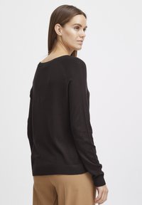Pull noir à manches longues avec un col rond et des poignets côtelés, vu de dos. Texture douce et coupe décontractée.