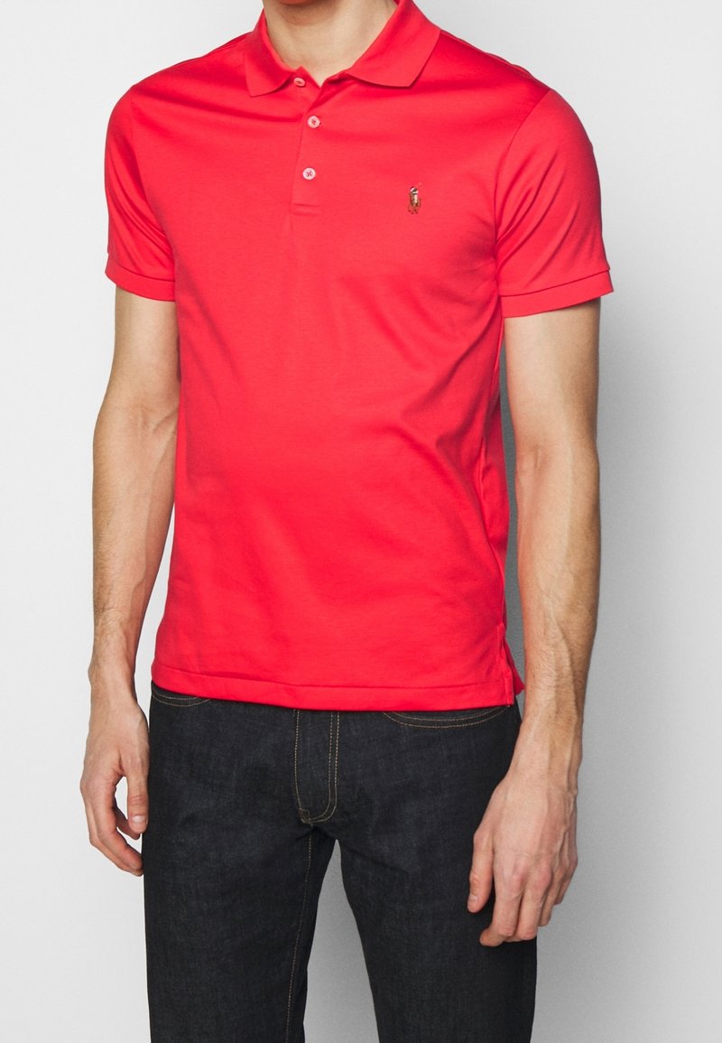 Rotes Poloshirt aus weicher Baumwolle mit klassischem Kragen, kurzen Ärmeln, einer Knopfleiste mit drei Knöpfen und kleinem Logo auf der Brust.