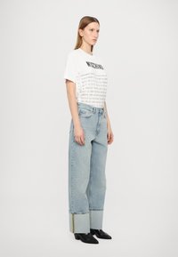 T-shirt branca com texto impresso em preto; combinada com jeans de pernas largas em azul claro com a bainha dobrada e costura multicolorida. Botas de salto pretas.
