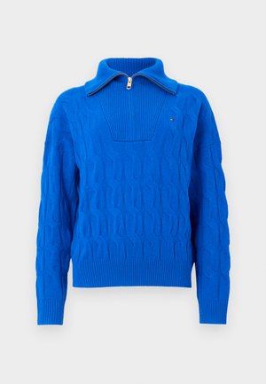 Suéter em ponto canelado azul brilhante, com mangas longas e gola com meia zipper, em fundo branco.