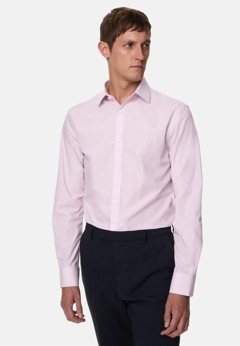 Lichtroze blouse met lange mouwen, een kraag met knoopsluiting, effen stof en witte knopen, gecombineerd met donkere broeken. Soepele textuur.