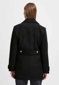 Manteau en laine noire au design épuré, grand col et boutons argentés à la taille et aux manches, arborant une texture solide.