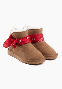 Stivaletti in suede marrone con fodera in pelliccia bianca, caratterizzati da un bandana rosso annodato intorno alla caviglia. Suola in gomma spessa per una maggiore durata.