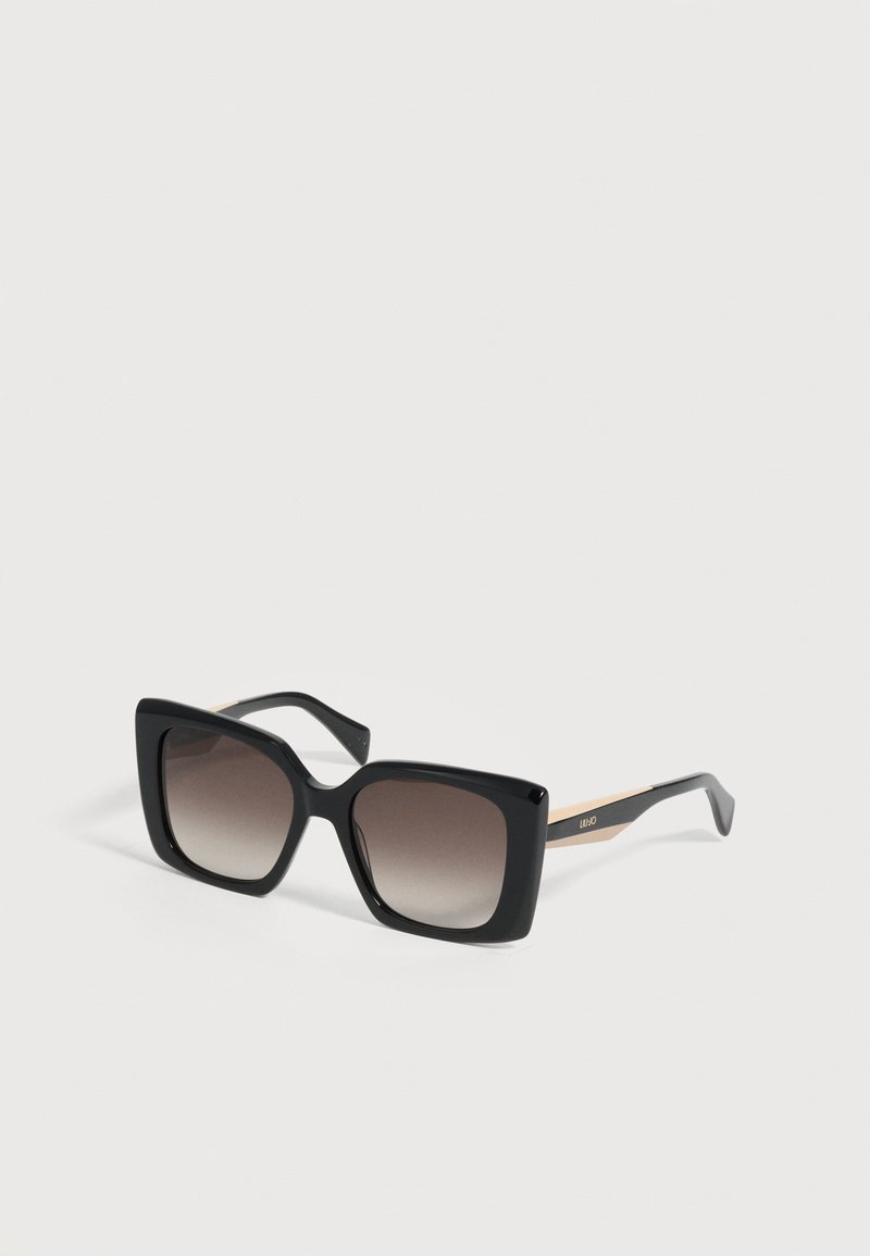 Lunettes de soleil carrées oversize noires avec des verres dégradés foncés et des branches accentuées d’or, marquées « Liu Jo » sur un côté.