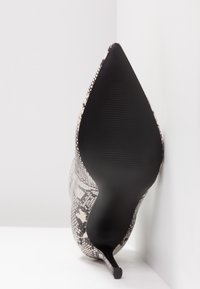 Chaussure à talon stiletto à bout pointu avec semelle noire et dessus imprimé serpent gris, vue de dessous en angle sur un fond blanc d’angle.