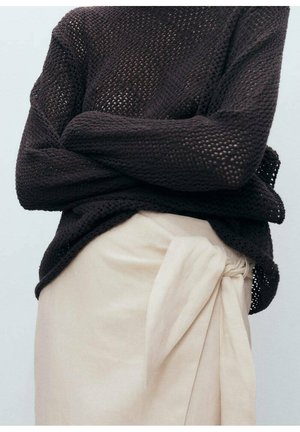 Tumma neulepaita, jossa on avara kudonta, yhdistettynä vaaleaan kietaisuhameeseen, jossa on kankainen rusetti yksityiskohtana sivussa.