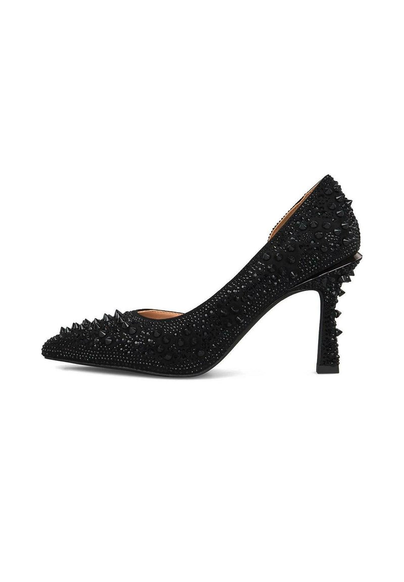 Zapato de tacón alto negro con punta afilada, adornado con brillantes remaches negros y un detalle texturizado en la superficie, con un tacón decorativo con picos.