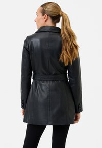Black leather coat with a belted waist, sharp lapels, and buttoned cuffs. Smooth texture with a tailored fit, reaching mid-thigh.