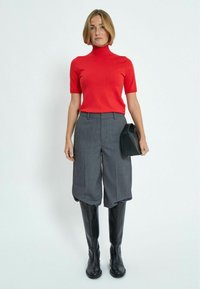 Suéter corto de manga corta y cuello alto rojo, combinado con pantalones cortos de pierna ancha de tiro alto gris, y acompañado de un bolso negro y botas altas negras.