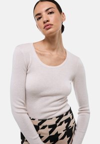 Haut rose clair à manches longues avec un décolleté à arrondi, fabriqué en tissu texturé, associé à une jupe à motif pied-de-poule noir et crème.