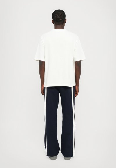 Camiseta blanca de manga corta combinada con pantalones azul marino que cuentan con franjas blancas laterales, de corte relajado y una textura de algodón suave.