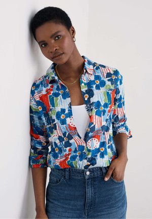 Colorful floral button-up shirt with blue, red, and green patterns, paired with fitted blue jeans. Smooth fabric and rolled sleeves.
