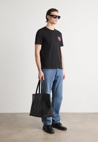 Black short-sleeve t-shirt with red heart logo, blue jeans, black leather shoes, and a soft black tote bag with embossed lettering.