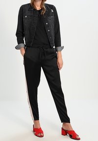 Sort denimjakke med knaplukning og optrillede ærmer, sorte tapered bukser med pink striber i siden, og røde sandaler med blokhæle.