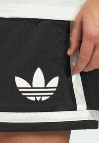 Black athletic shorts made of perforated fabric, featuring a white Adidas trefoil logo and white trim along the hem and side.