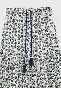 Weißer Stoffrock mit einem marineblauen Blättermuster, elastischem Bund mit dekorativen Bändern und Quasten sowie einem Rüschensaum.