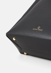 Sac en cuir noir texturé avec des accents en métal doré, présentant une forme structurée et un logo en relief bien visible sur le devant.