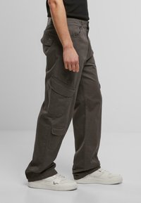 Grå cargo bukser med flere sidelommer, rett snitt og mykt bomullsmateriale, brukt med hvite sneakers og svart topp.
