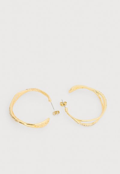 Uhani z odprtimi obroči v zlati barvi z teksturiranim vzorcem in majhnimi vgrajenimi kristali, prikazani z metalnimi zatiči in sijočimi zatiči v obliki metulja na belem ozadju.