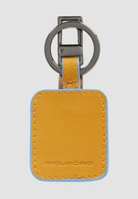 Leren sleutelhanger in helder geel met blauwe accenten en stiksel. Voorzien van een cirkelvormige metalen ring voor bevestiging en geperste details.