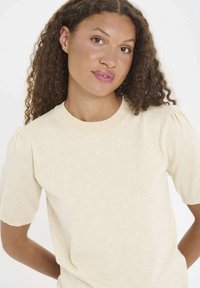 Beige short-sleeve top with a round neckline and puffed shoulder seams. Soft, textured fabric with a slightly relaxed fit. Minimalist design.