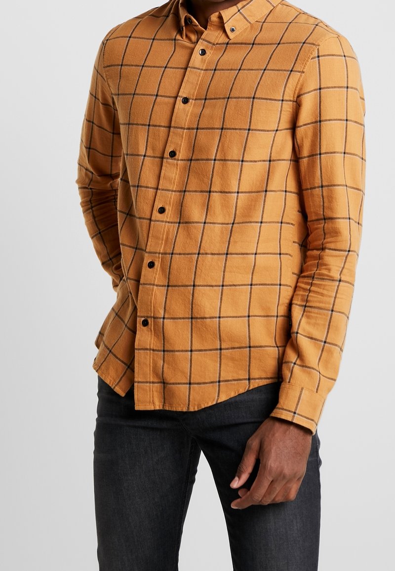 Camicia in flanella gialla senape con motivo a quadri neri, colletto button-down, maniche lunghe e cinque bottoni neri sulla parte anteriore.