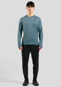 Mouwloze, teal sportshirt met een gestructureerd patroon en een ronde halslijn, gecombineerd met zwarte tapered broek met accenten en logo's.