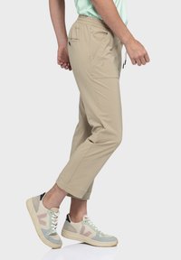 Beige, leichte Hosen mit einem elastischen Bund, seitlichen Taschen und einem taillierten Design, kombiniert mit mehrfarbigen, nachhaltigen Sneakers.