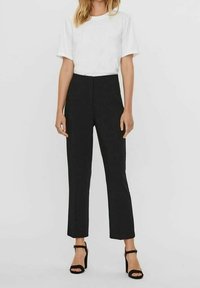 Camiseta blanca de manga corta combinada con pantalones ajustados negros, con un corte recto y diseño elegante, complementados con sandalias de tacón negras.