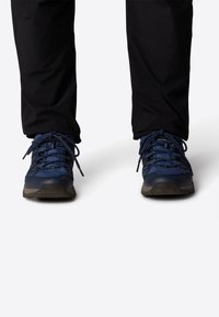 Siniset vaelluskengät, joissa on verkkokangasta ja kumimateriaalia, ja joissa on tekstuuriset yksityiskohdat sekä tukevat nauhat. Pohja on suunniteltu tarjoamaan pitoa.