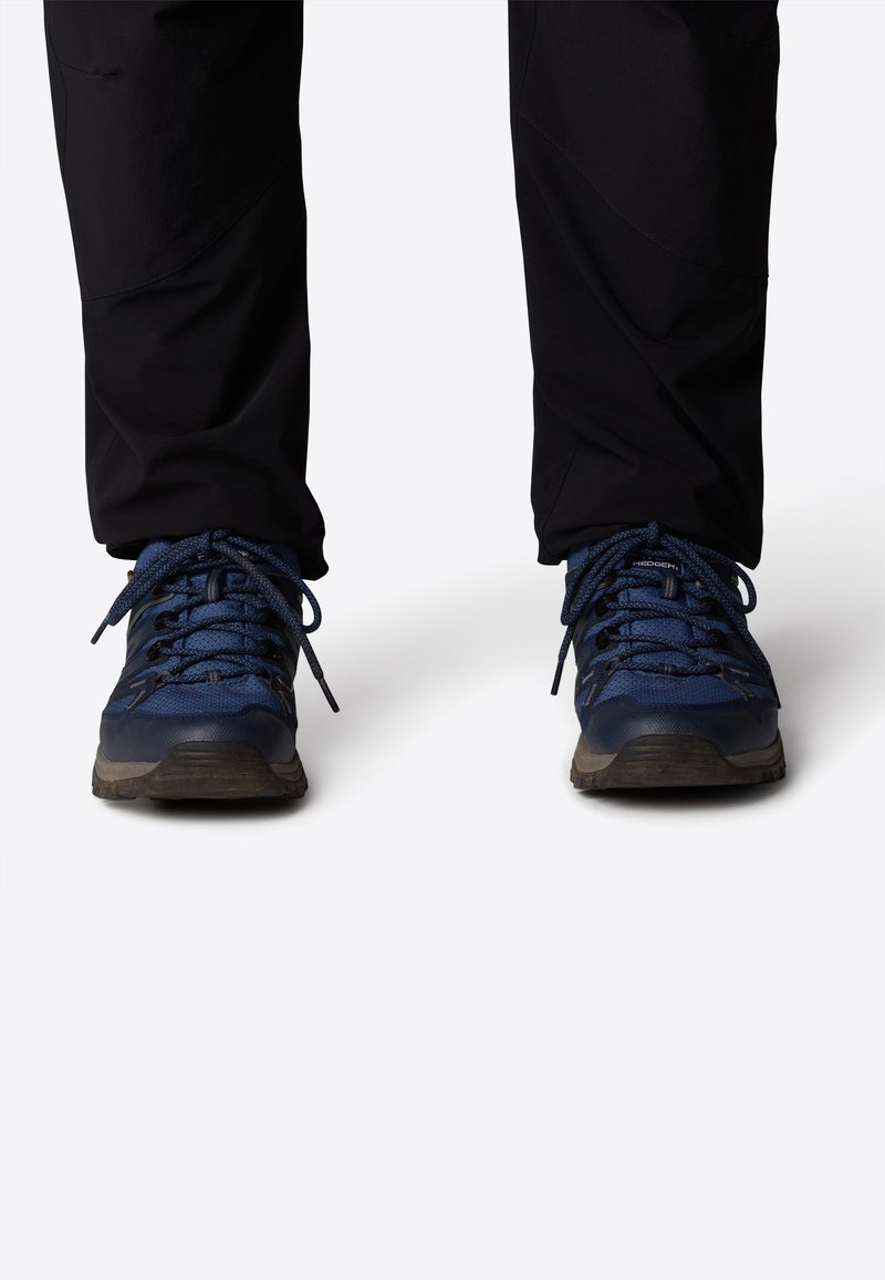 Siniset vaelluskengät, joissa on verkkokangasta ja kumimateriaalia, ja joissa on tekstuuriset yksityiskohdat sekä tukevat nauhat. Pohja on suunniteltu tarjoamaan pitoa.