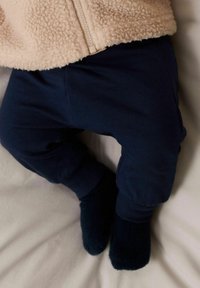 Pantalons de jogging navy en matériau doux avec des poignets côtelés, associés à des chaussettes navy foncé, placés sur une surface en tissu clair.
