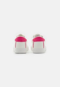 Hvite sneakers har en rosa teksturert hæltass og rosa aksentstripe. Glatt læraktig materiale, lavprofil-design og gummisåle.