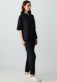 Schwarzes Leinenhemd mit Kragen und Knopfverschluss, kombiniert mit passenden schwarzen Hosen und weißen Turnschuhen. Schlicht, lässige Passform.