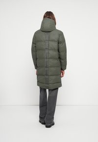 Olive roheline puffer mantel kapuutsiga, millel on vertikaalne must triip ja logo. Mantel on keskpika pikkusega ja sellel on tekstuuriga, tikitud välimus.