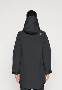 Parka negra con capucha, que presenta una textura suave, mangas largas, puños ajustables y un logo en el hombro derecho.