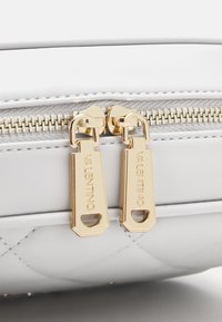 Fehér bőrtáska steppelt dizájnnal. Arany cipzárhúzók márkajelzéssel. Simább felület és fémbetétek.