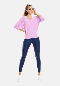 Helles Pink, lockere Bluse mit weiten Ärmeln, kombiniert mit dunklen, glänzenden Leggings in Navy und weißen Sportschuhen. Minimalistisches Design, glatte Textur.