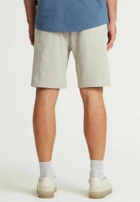 Pantaloni scurți gri deschis cu o textură netedă, având un brâu elastic și buzunare laterale, asortați cu adidași albi și șosete gri.