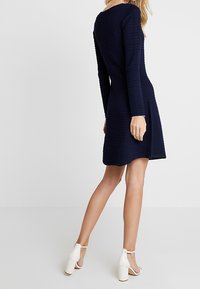 Robe en maille bleu marine à manches longues, tissu texturé, corsage ajusté, jupe évasée, et escarpins blancs à bride cheville.