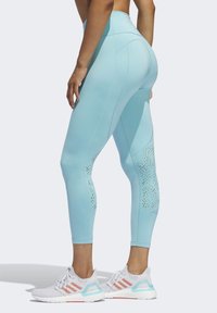 Leggings a vita alta di colore azzurro chiaro realizzati in tessuto elasticizzato, con dettagli di intaglio vicino alla parte inferiore delle gambe. Abbinati a scarpe da ginnastica bianche.