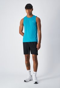 Turkusowy bezrękawnik sportowy z teksturowanej tkaniny, w zestawieniu z czarnymi szortami. Białe sneakersy i wzorzyste skarpetki dopełniają całość.