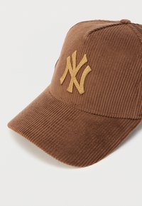 Brown corduroy baseball cap with a curved visor and a gold embroidered New York Yankees logo on the front. Textured fabric detail visible.