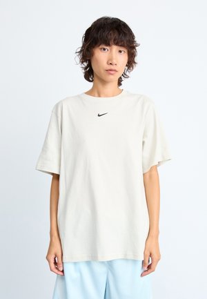 Svetlo bež T-shirt kratkih rukava od bombaža, s malim crnim Nike logotipom na prsima. Opusteni kroj s okruglim izrezom.