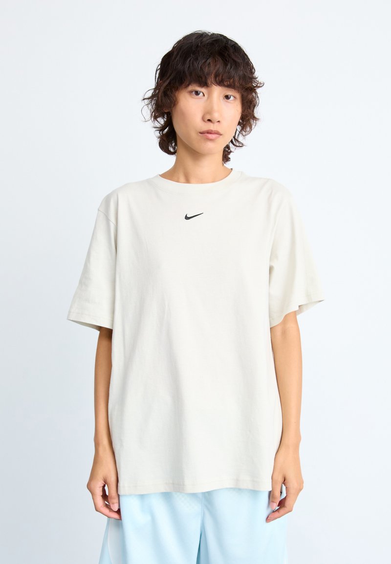 Šviesiai ruda trumpomis rankovėmis marškinėliai, pagaminti iš medvilnės, su mažuoju juodu Nike logotipu ant krūtinės. Laisvas siluetas su apvaliu iškirpimu.